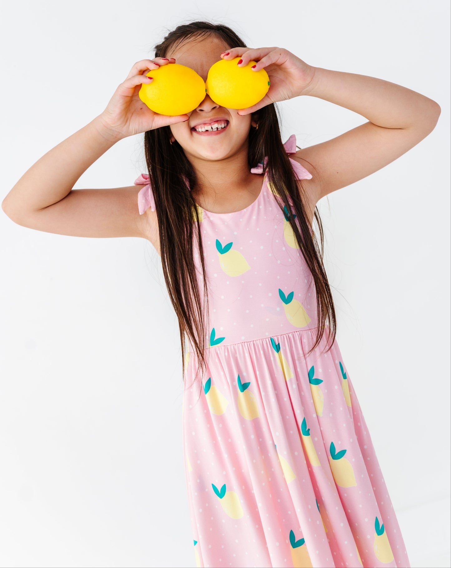 Child wearing a pink dress with lemon patterns, holding lemons over their eyes.