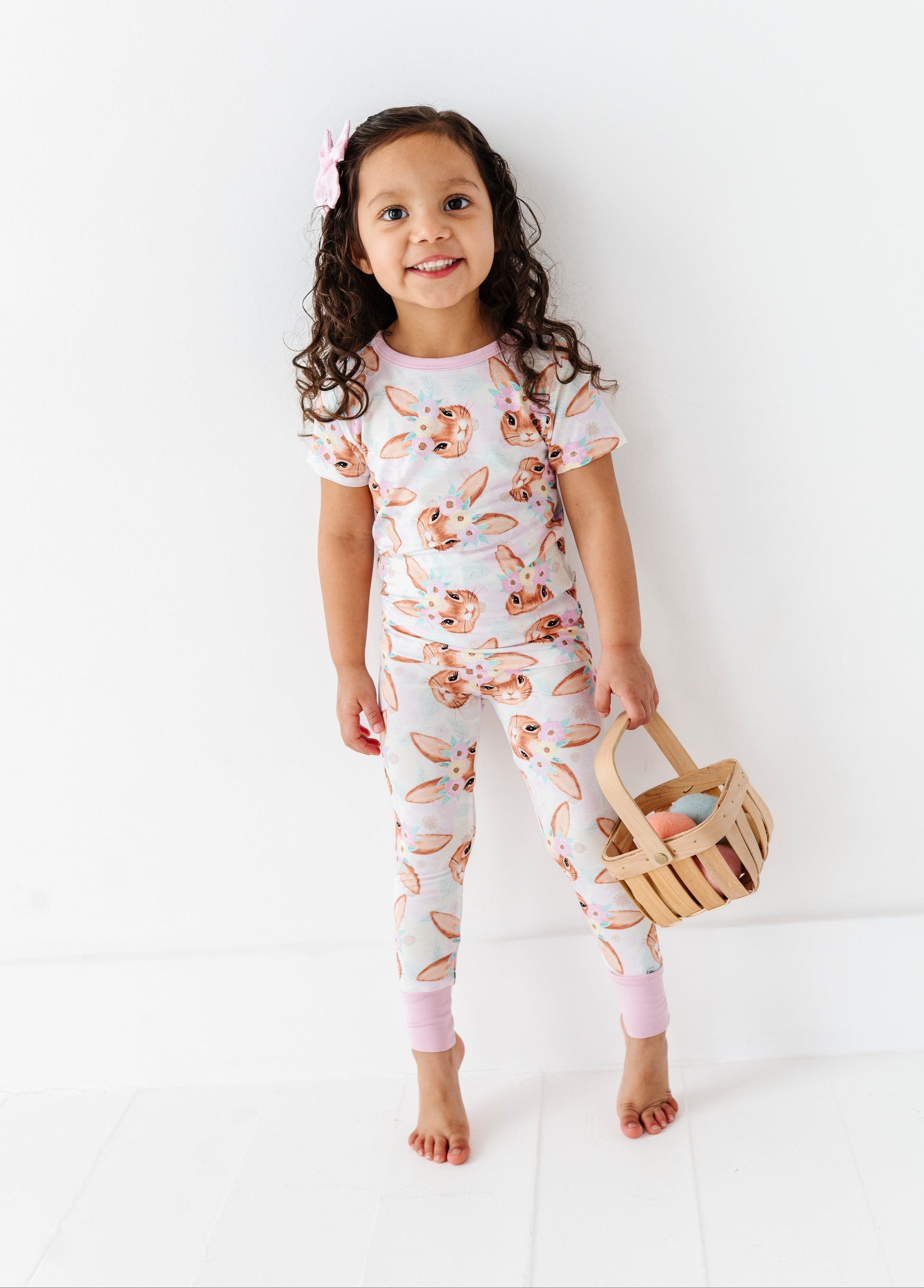 Child wearing a floral bamboo onesie holding a wooden basket on a white background