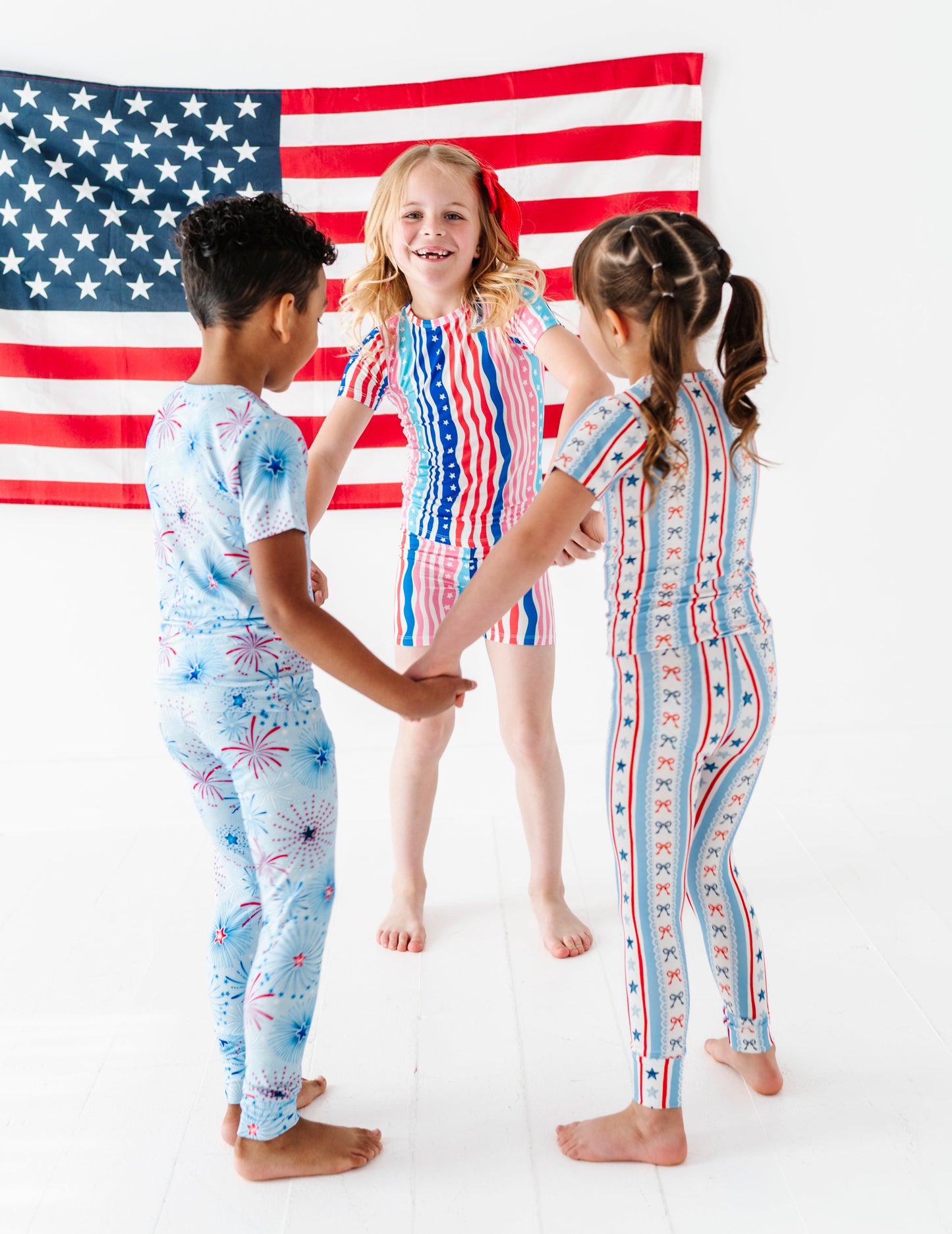 Three children in patriotic bamboo pajamas standing in front of an American flag.