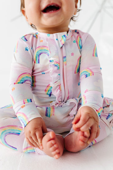 Child wearing a colorful watercolor rainbow-themed bamboo convertible romper on a white background
