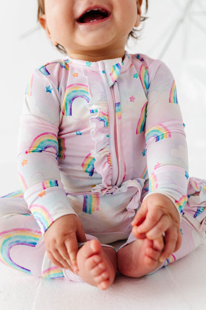 Child wearing a colorful watercolor rainbow-themed bamboo convertible romper on a white background