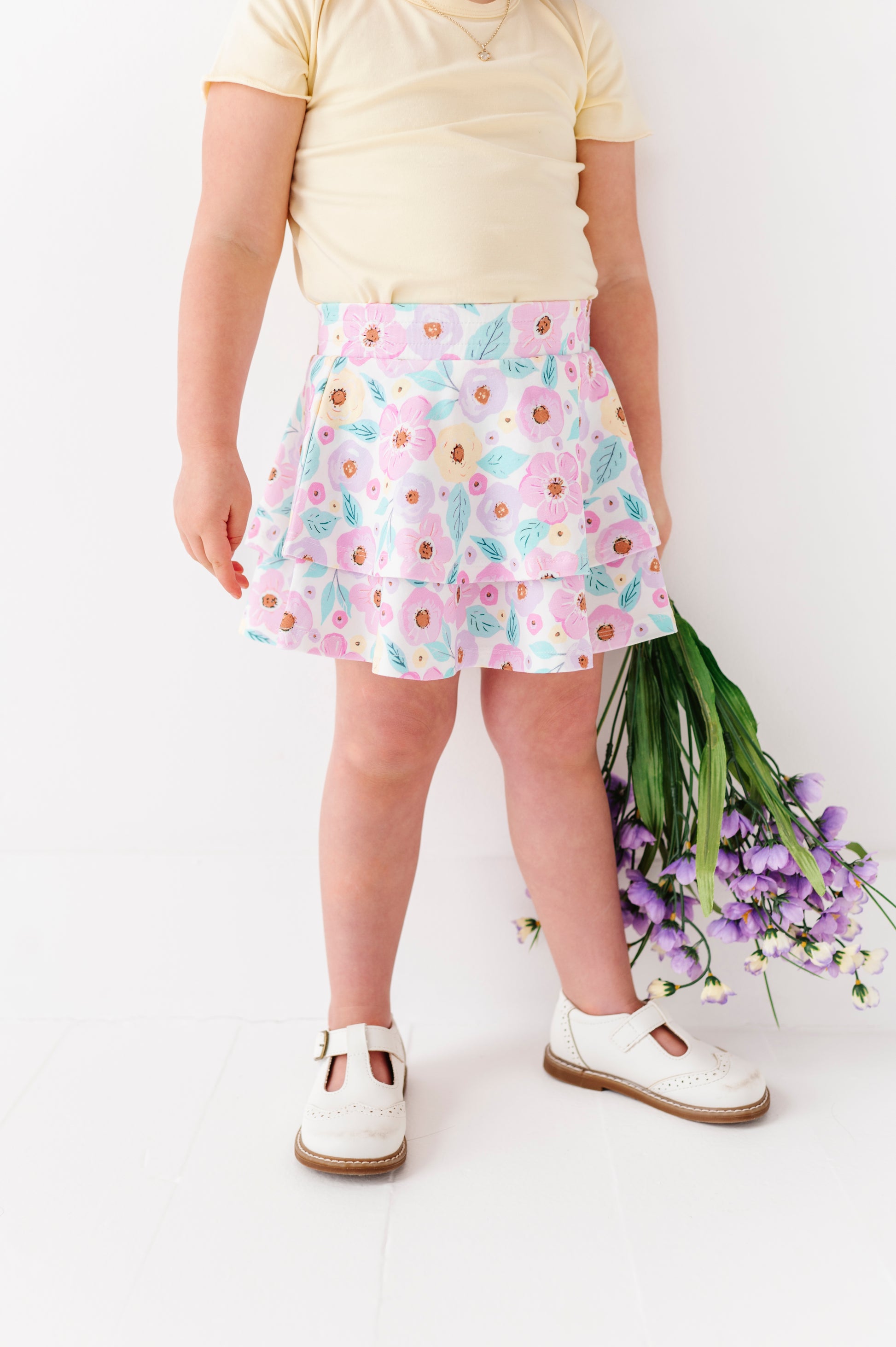 Child wearing a floral skort holding flowers on a white background