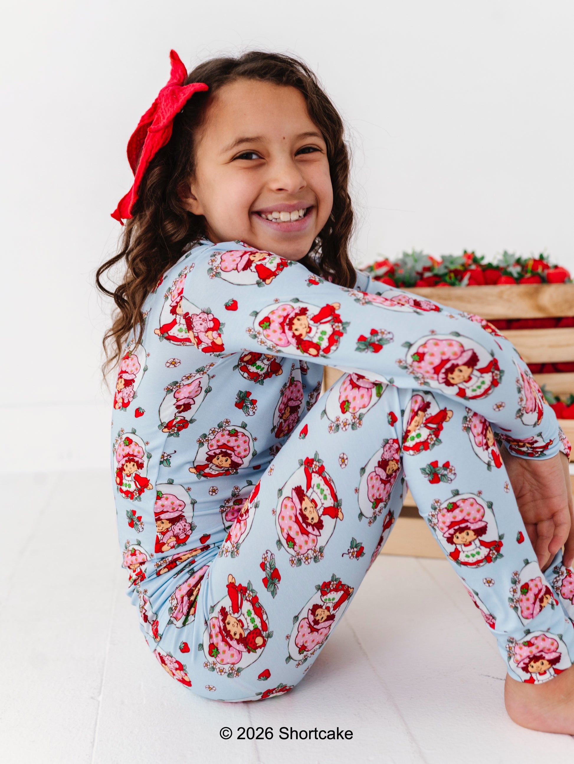 Child wearing an officially licensed Strawberry Shortcake™ pajama set with a red bow, sitting on a white background.