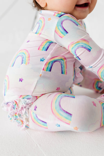 Baby wearing a bamboo zip romper with rainbow pattern on a plain background