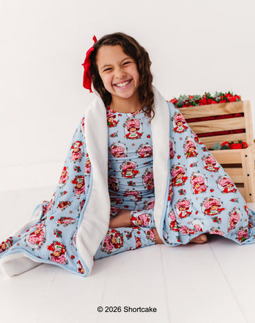 Girl wrapped in a Strawberry Shortcake™ bamboo blanket, sitting on a white floor.