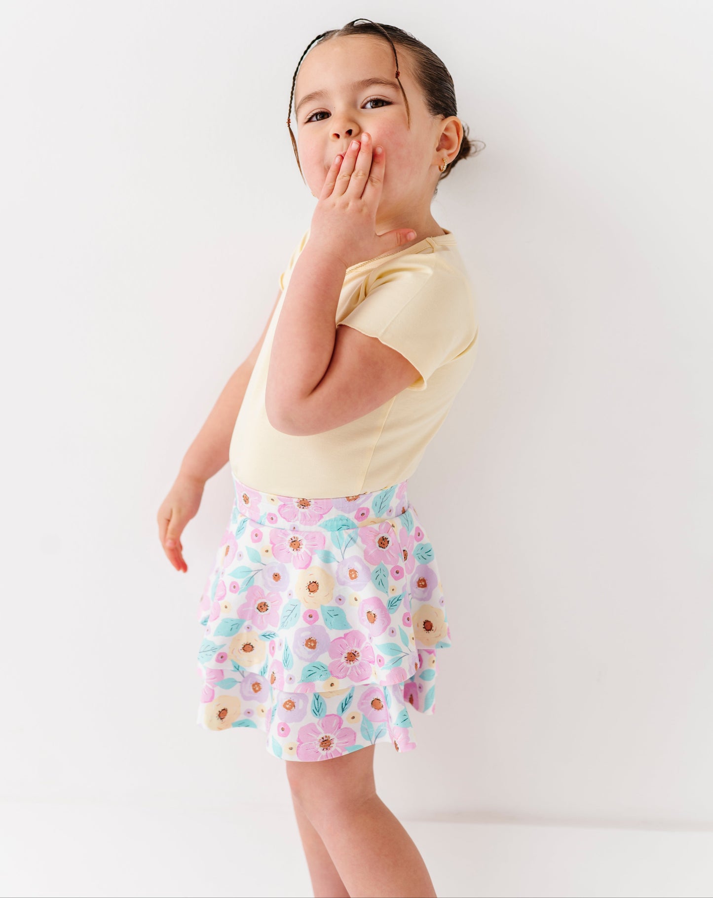 Child wearing a yellow shirt and floral skort on a white background