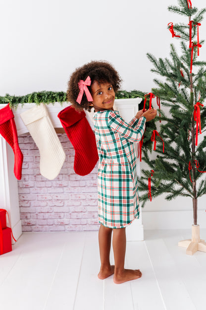 A little girl wearing a bamboo nightgown in a classic Christmas plaid print, decorating a Christmas tree