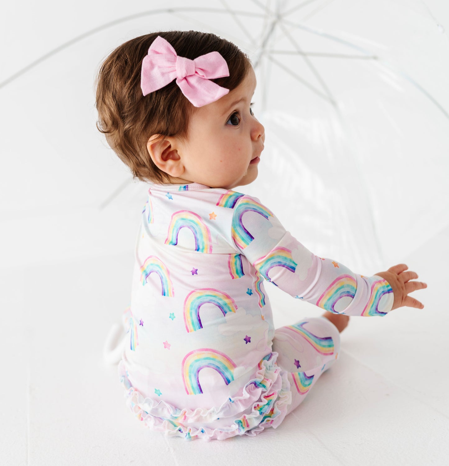 Baby wearing a rainbow bamboo convertible romper  with a pink bow on a white background