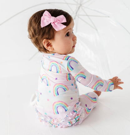 Baby wearing a rainbow bamboo convertible romper  with a pink bow on a white background