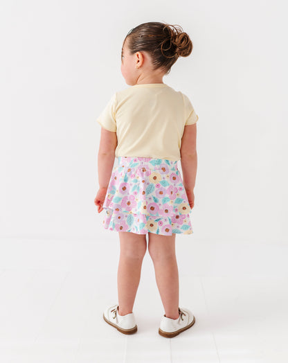 Child wearing a light yellow shirt and floral skort on a white background