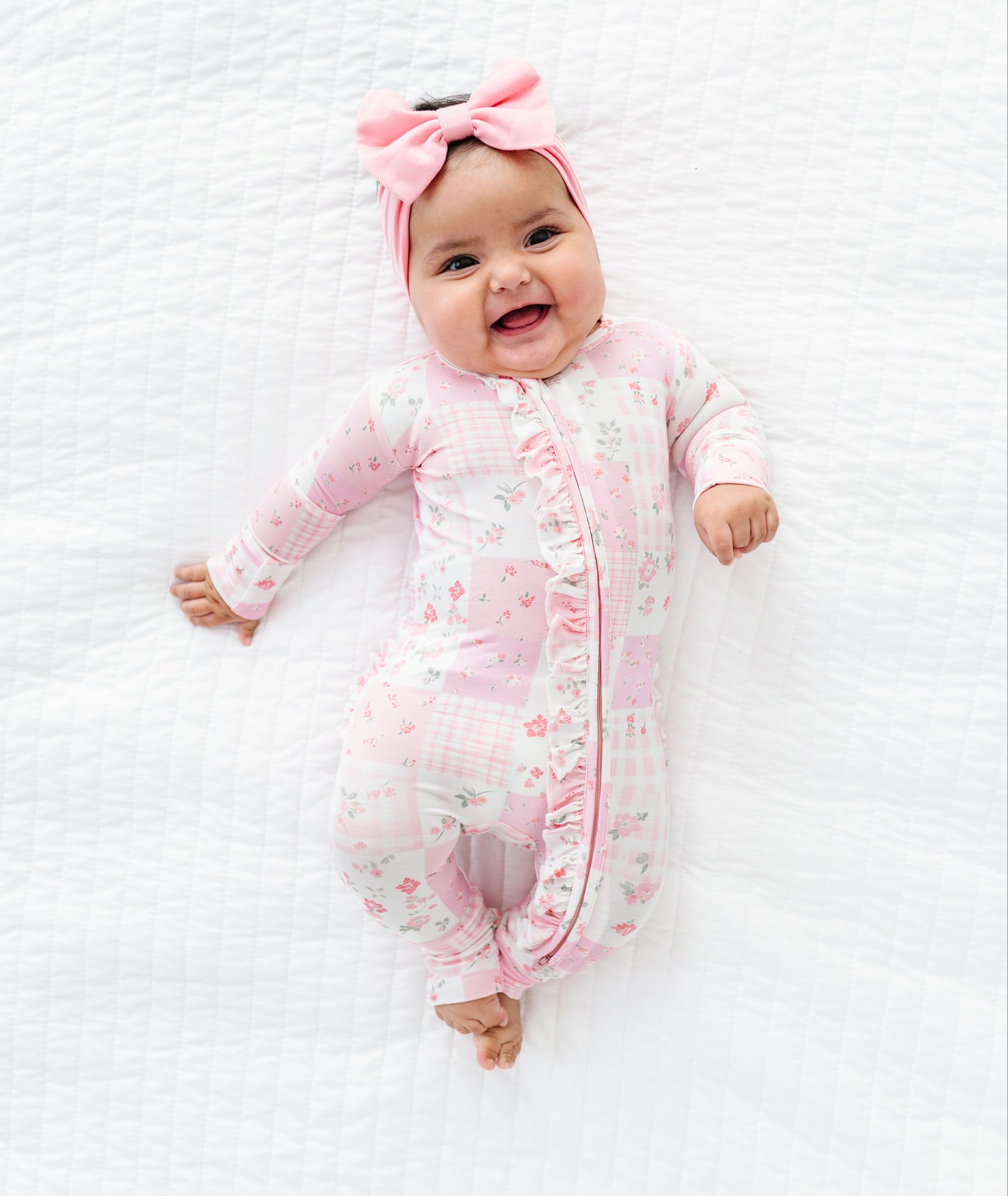 Baby in a pink floral bamboo convertible romper with a matching headband on a white textured background