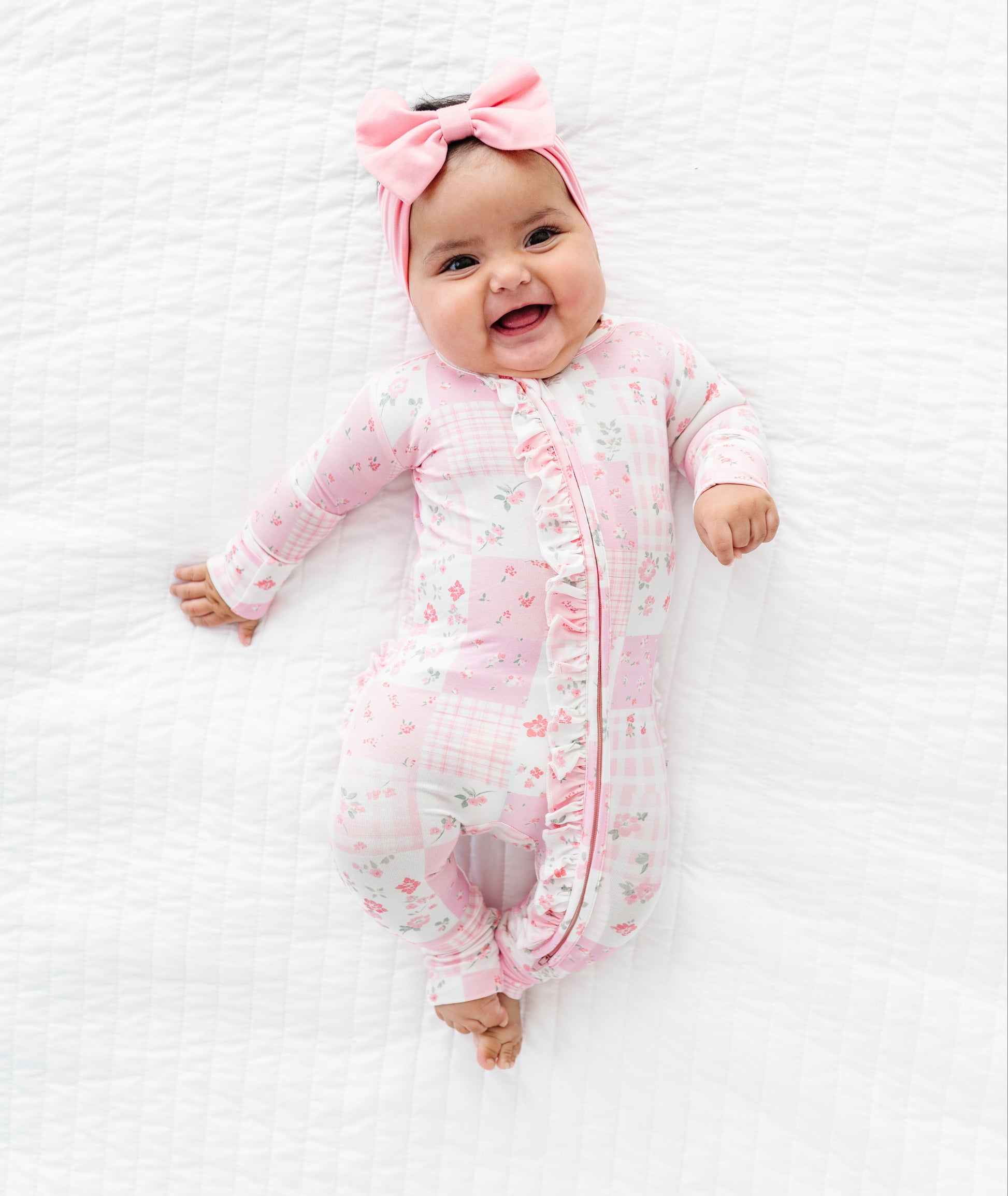 Baby in a pink floral bamboo convertible romper with a matching headband on a white textured background