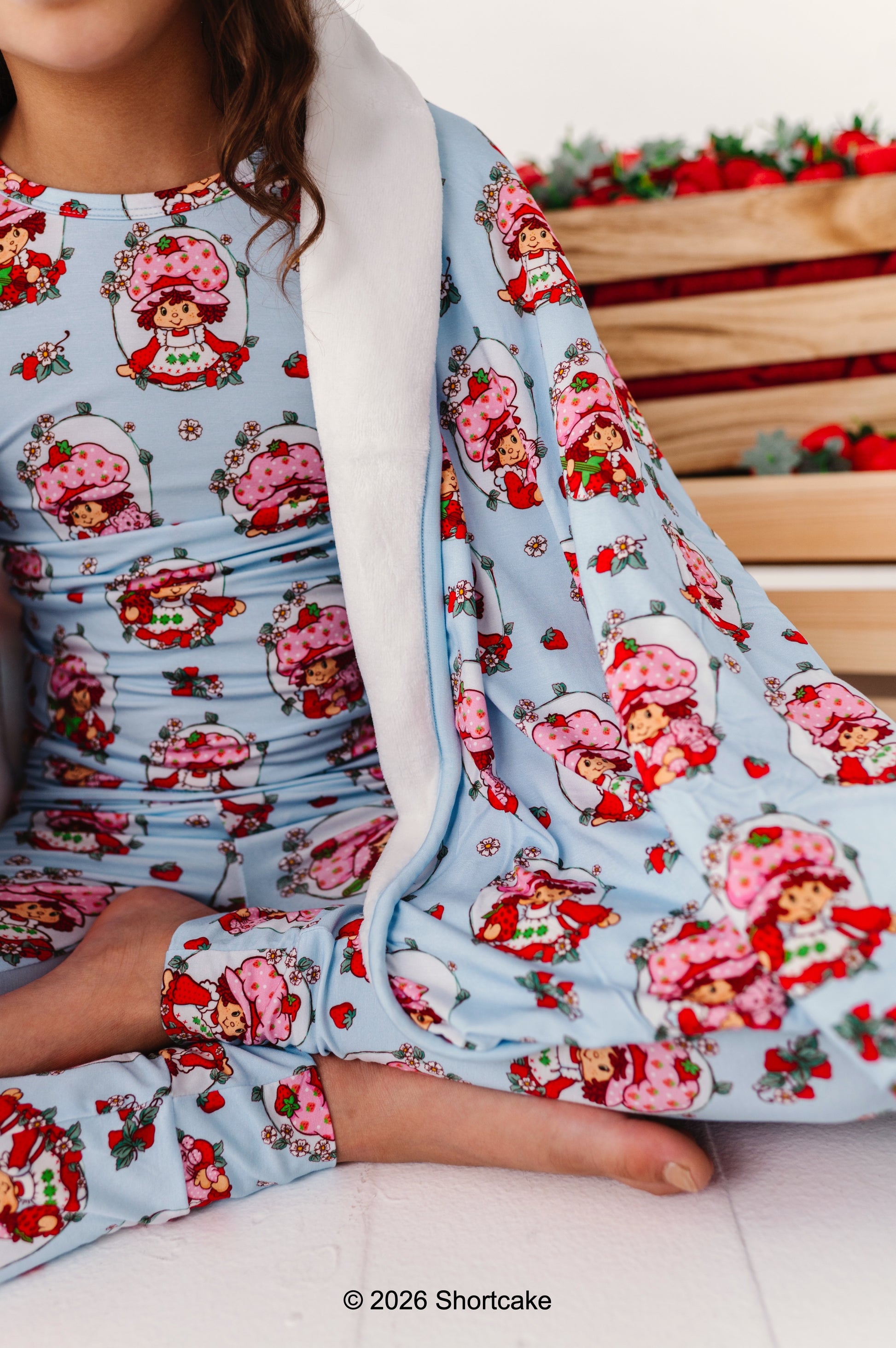 Little girl wearing licensed bamboo Strawberry Shortcake™ pajamas, wrapped in a Strawberry Shortcake™ plush bamboo blanket 