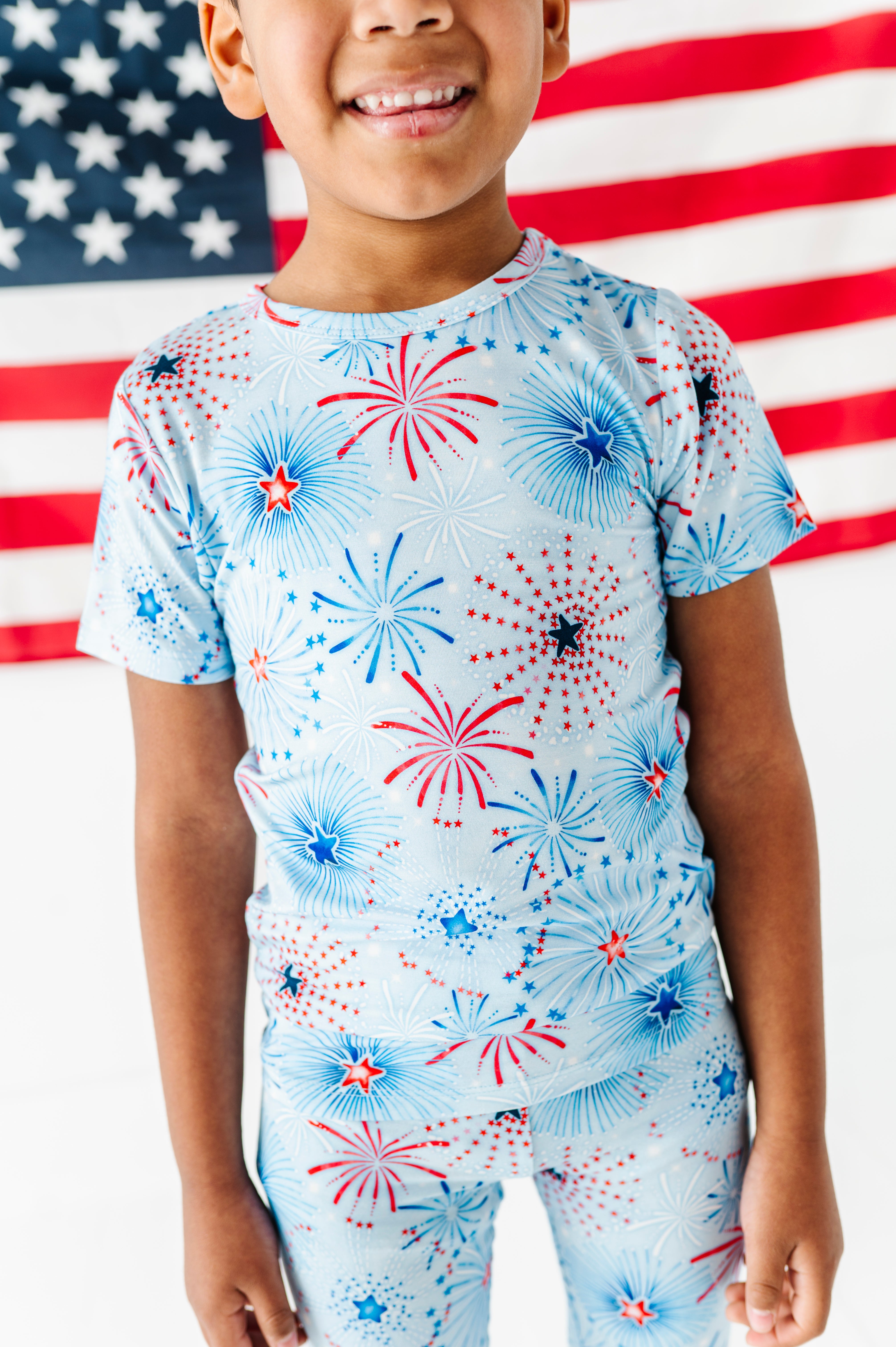 Child wearing a bamboo two-piece pajama set with fireworks pattern in front of an American flag