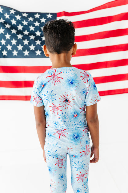 Child wearing a bamboo pajama set with fireworks design in front of an American flag
