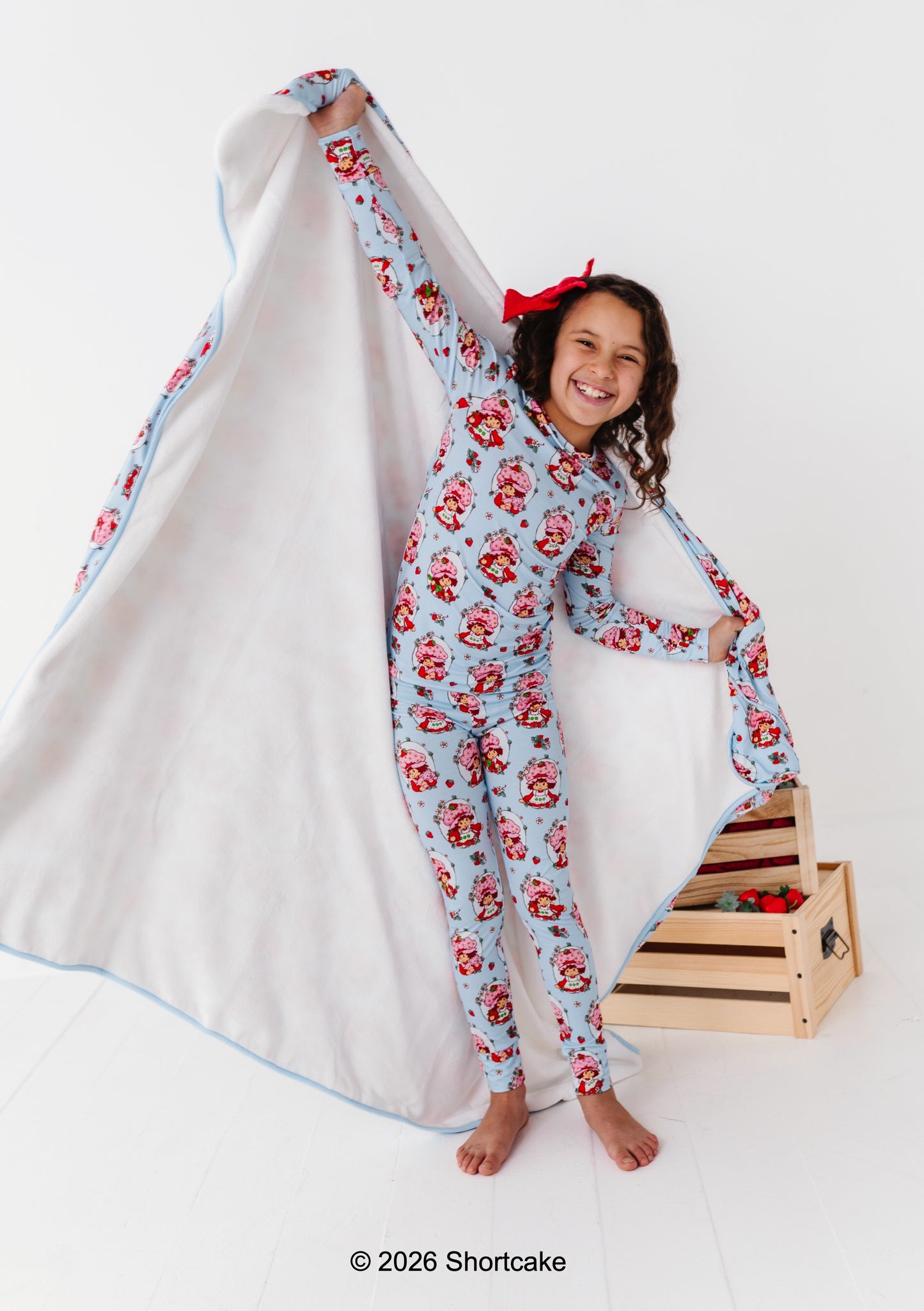 Girl in Strawberry Shortcake™ bamboo pajamas holding a coordinating licensed blanket with a white background