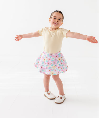 Child wearing a yellow top and floral skort on a white background