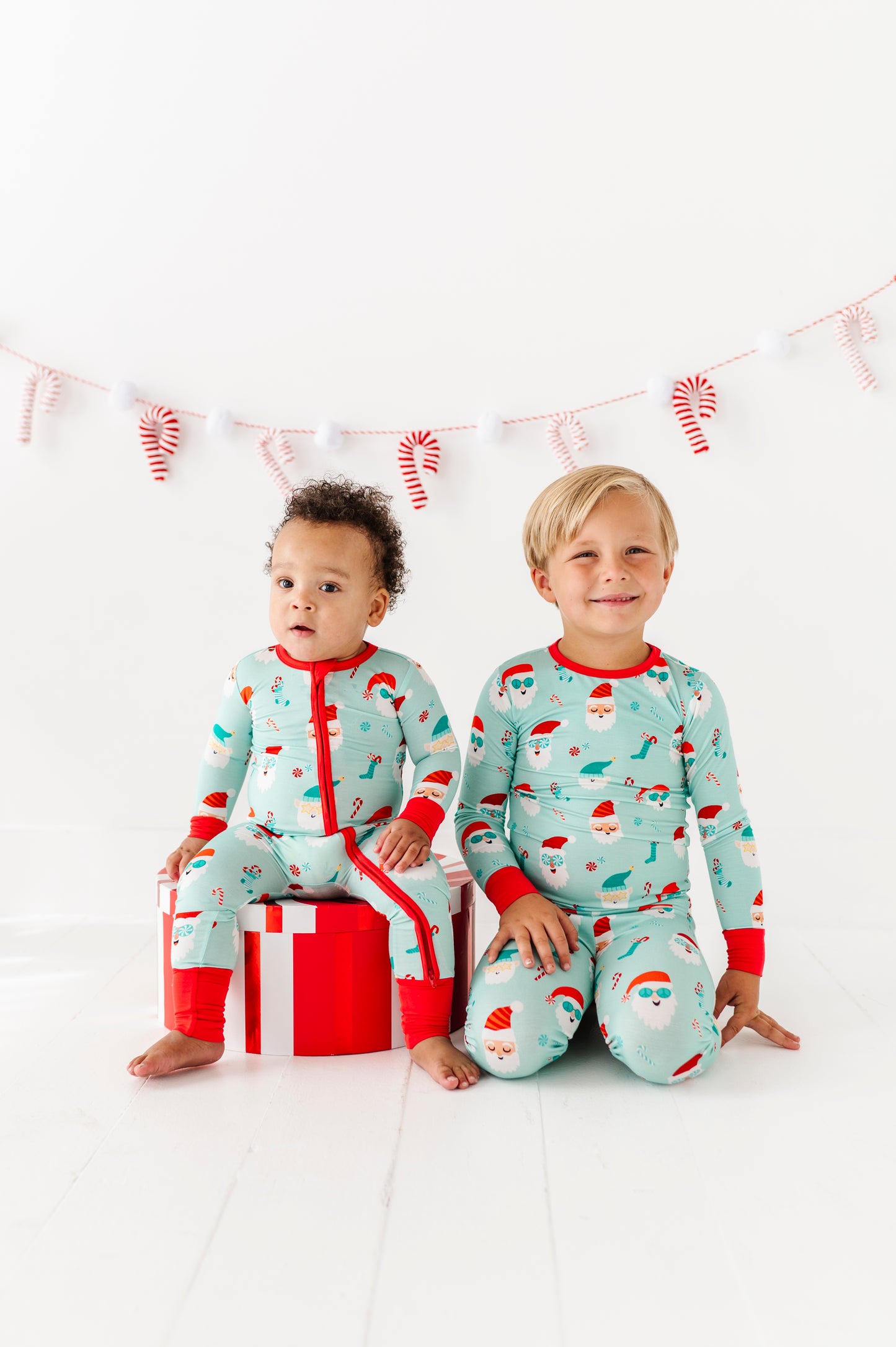 Two children wearing Christmas-themed bamboo pajamas sitting on a white background with candy cane decorations.
