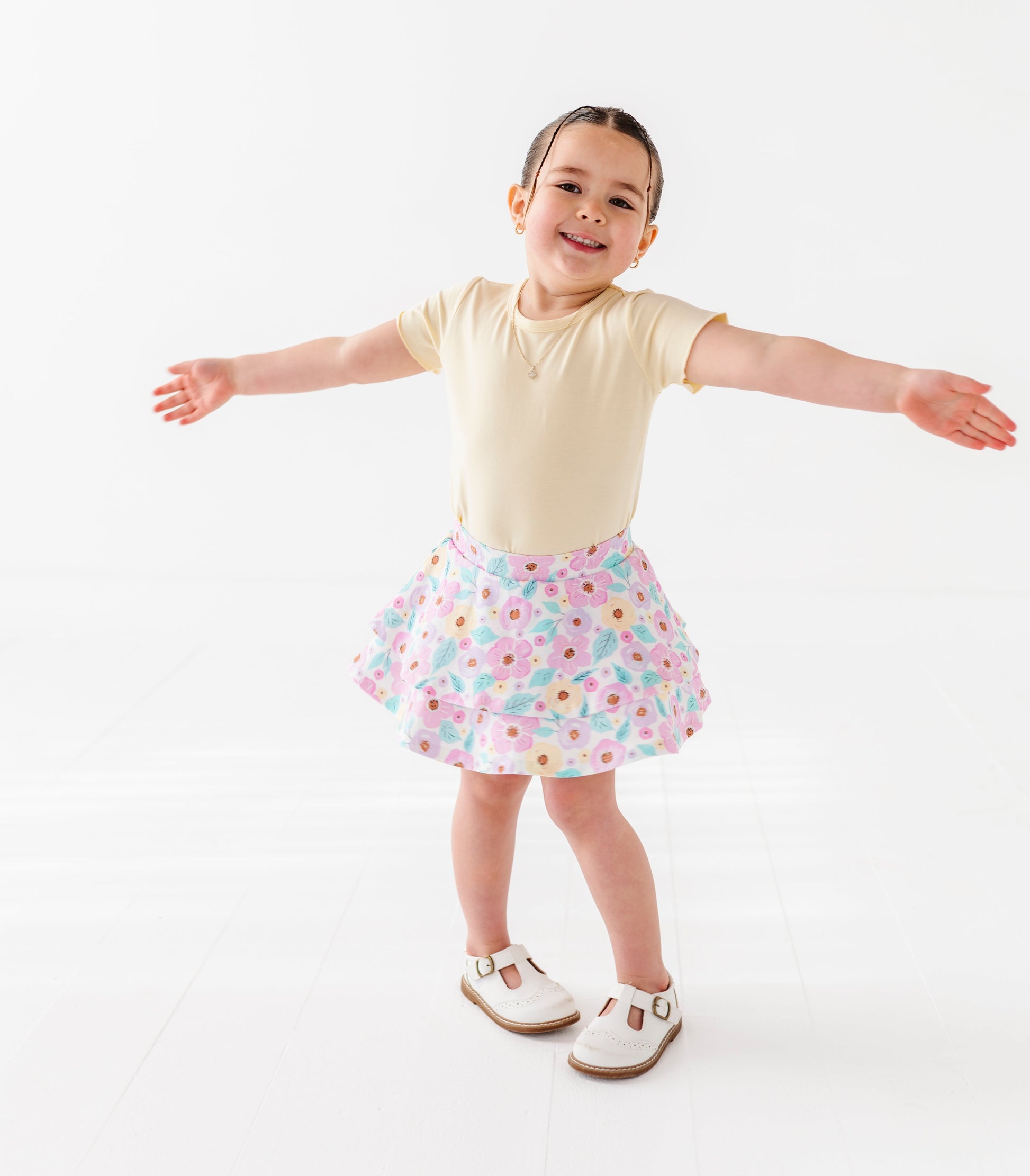Child wearing a yellow top and floral skort on a white background
