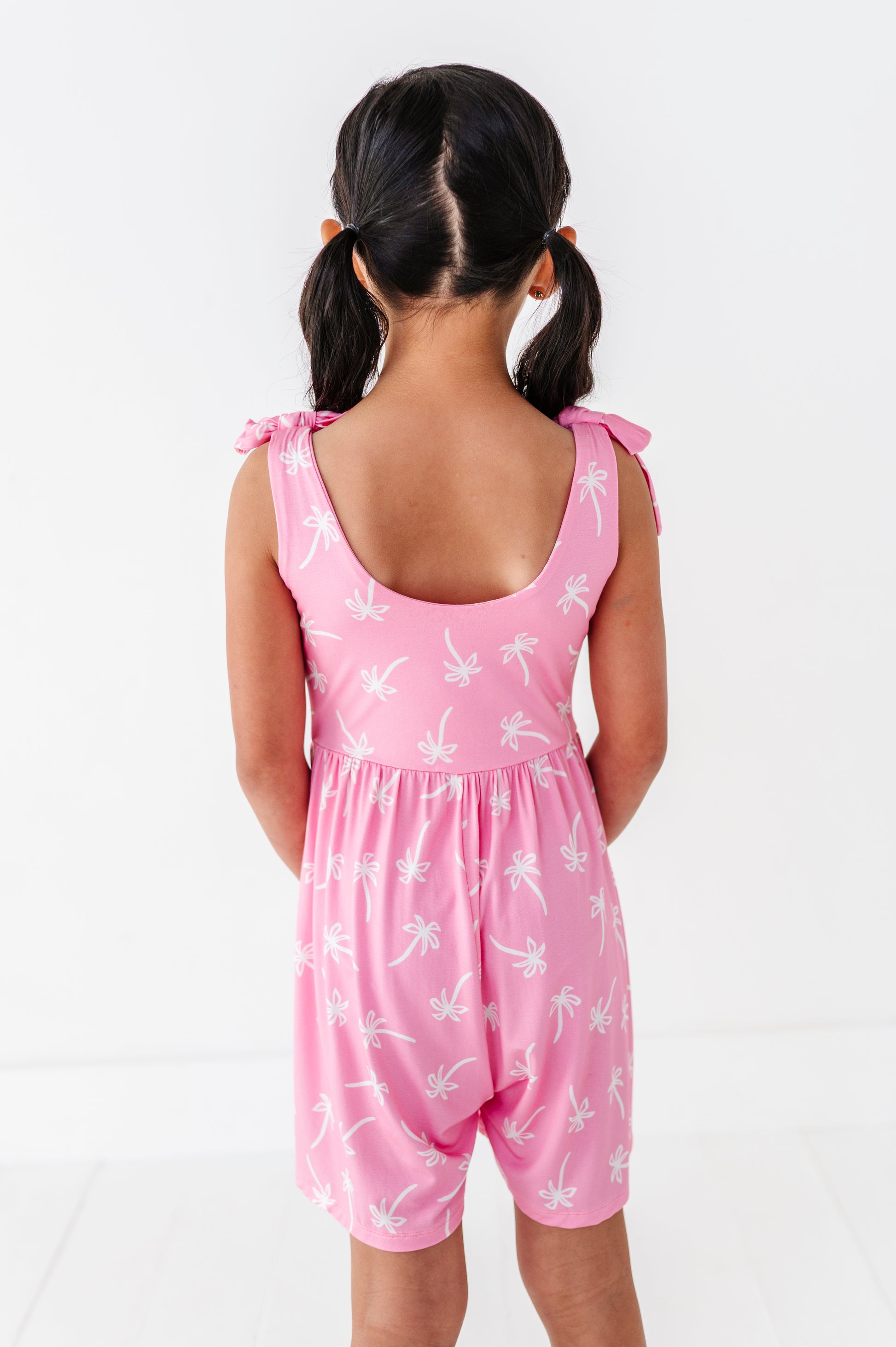 Young girl wearing a pink romper with white patterns on a white background