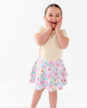 Child wearing a yellow top and floral skirt on a white background