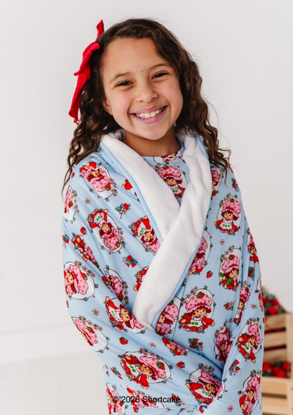 Child wrapped in a Strawberry Shortcake™ plush bamboo blanket, smiling against a plain background