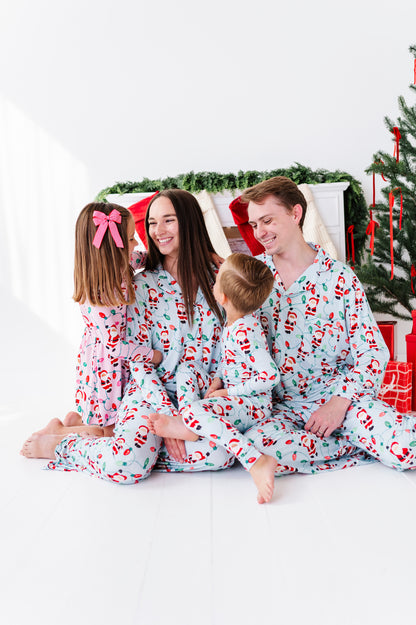 A family of four wearing matching light blue Christmas-themed bamboo pajamas with a red and green Santa Claus and candy cane print, sitting together in a brightly lit holiday setting with a Christmas tree and stockings in the background.