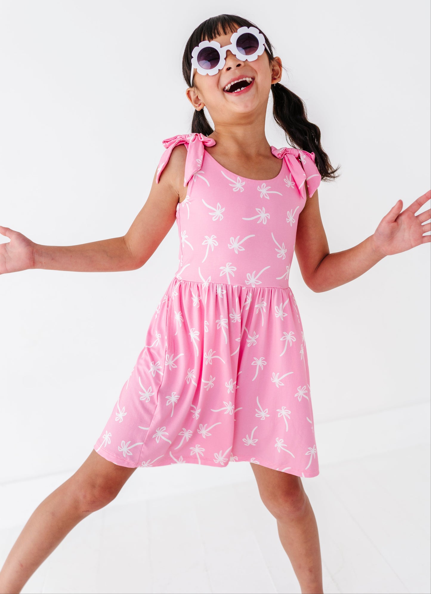 Young girl wearing a pink romper with white palm trees and sunglasses on a white background