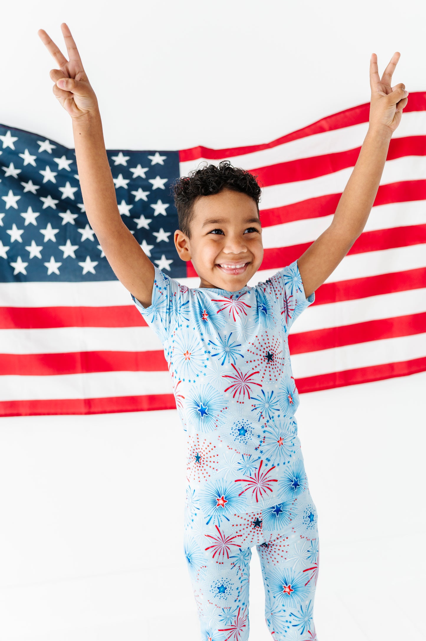 Child wearing a bamboo two-piece pajama set with fireworks design in front of an American flag