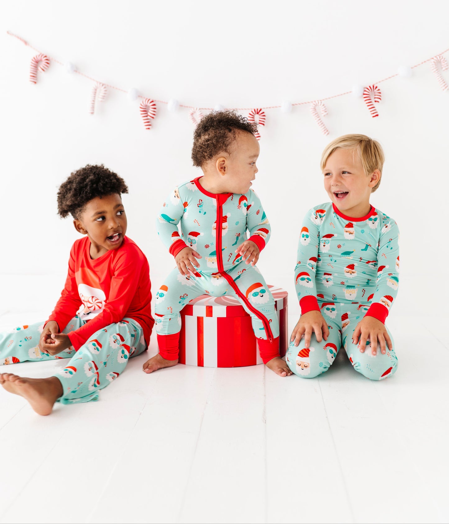 Three children wearing festive bamboo pajamas sitting together on a white background with candy cane decorations.
