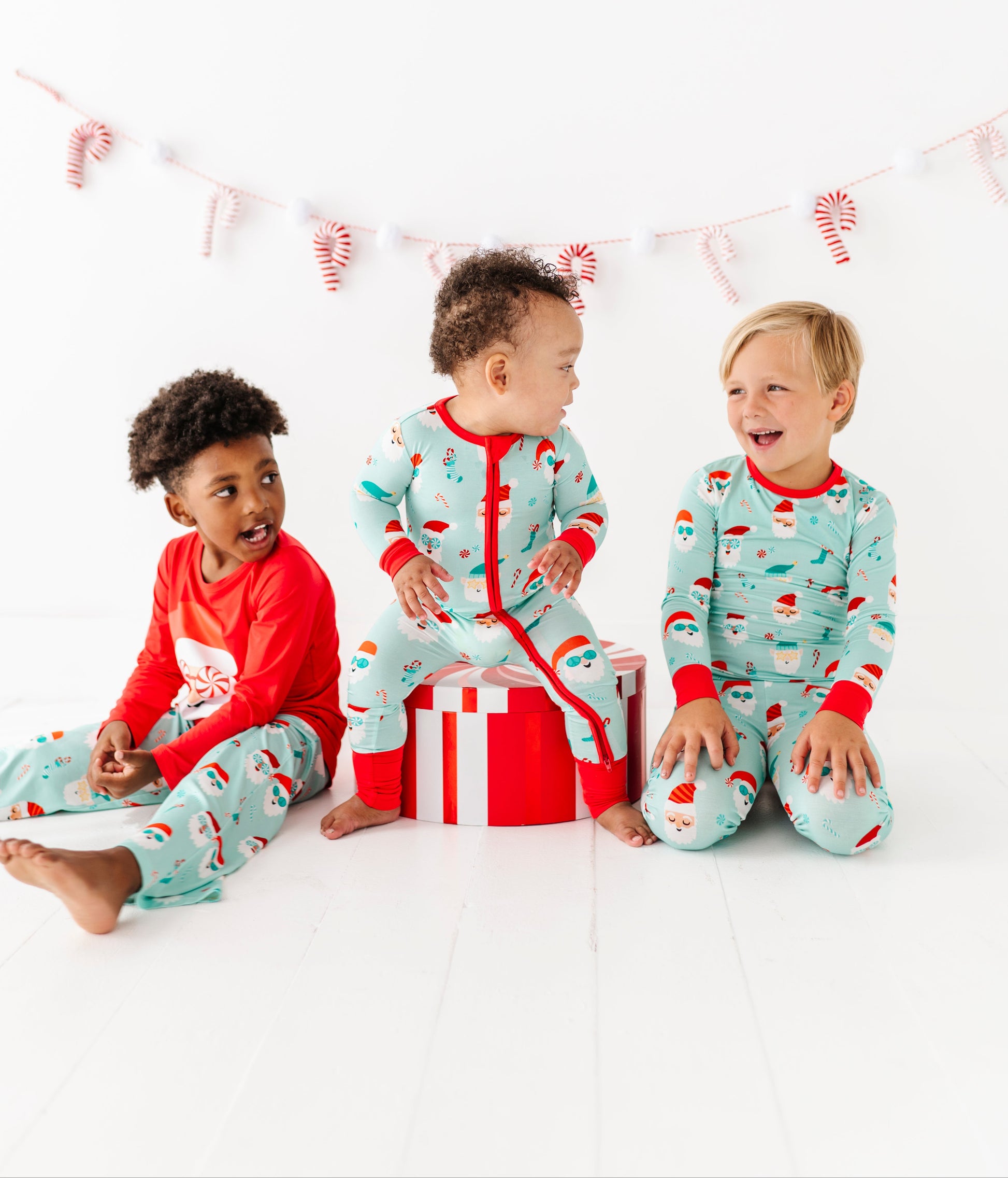 Three children wearing festive bamboo pajamas sitting together on a white background with candy cane decorations.