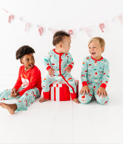 Three children wearing festive bamboo pajamas sitting together on a white background with candy cane decorations.