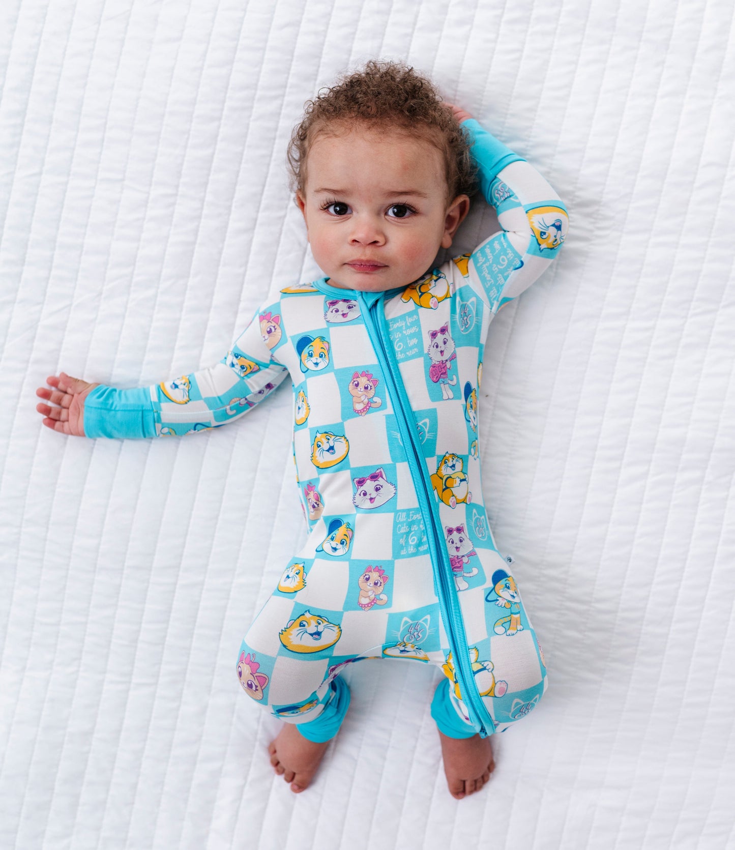 Baby wearing a colorful bamboo romper with cartoon 44 Cats characters on a white textured surface