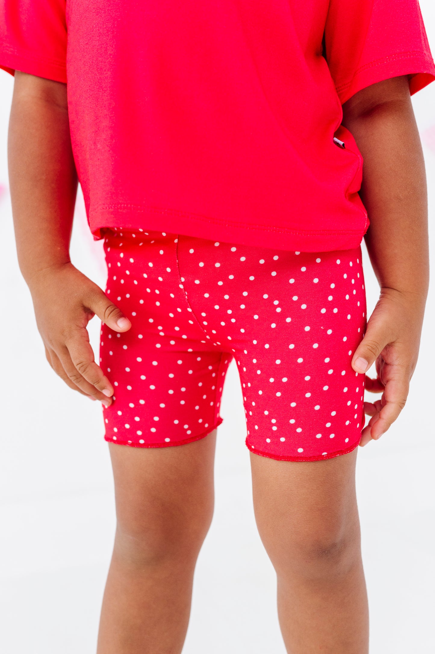 Child wearing red polka dot shorts and a red shirt on a white background