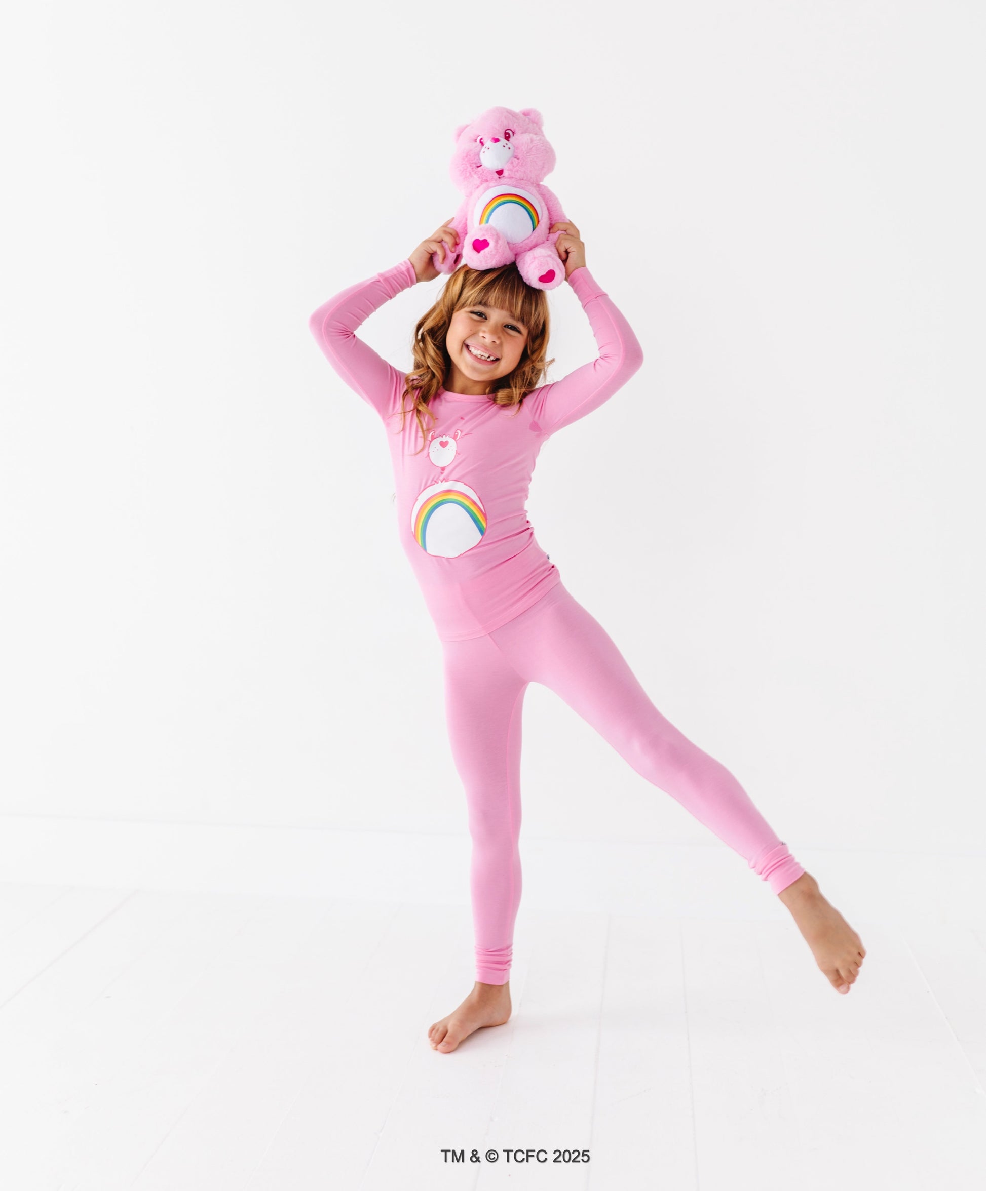 Kid smiling in pink Care Bears Cheer Bear pajamas on white background