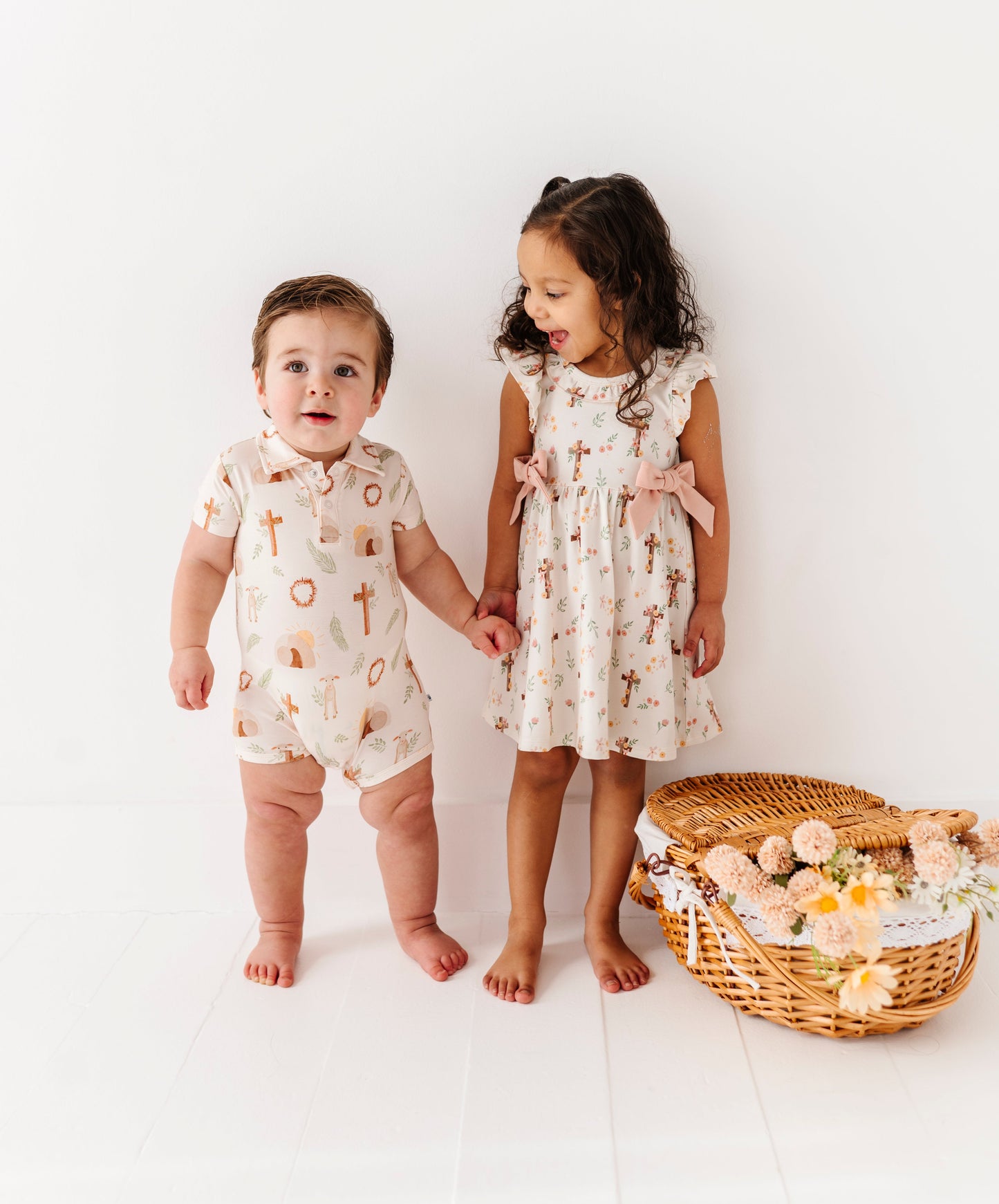 Two children wearing bamboo Easter daywear standing next to a basket of flowers on a white background, focused on Christianity and Jesus 