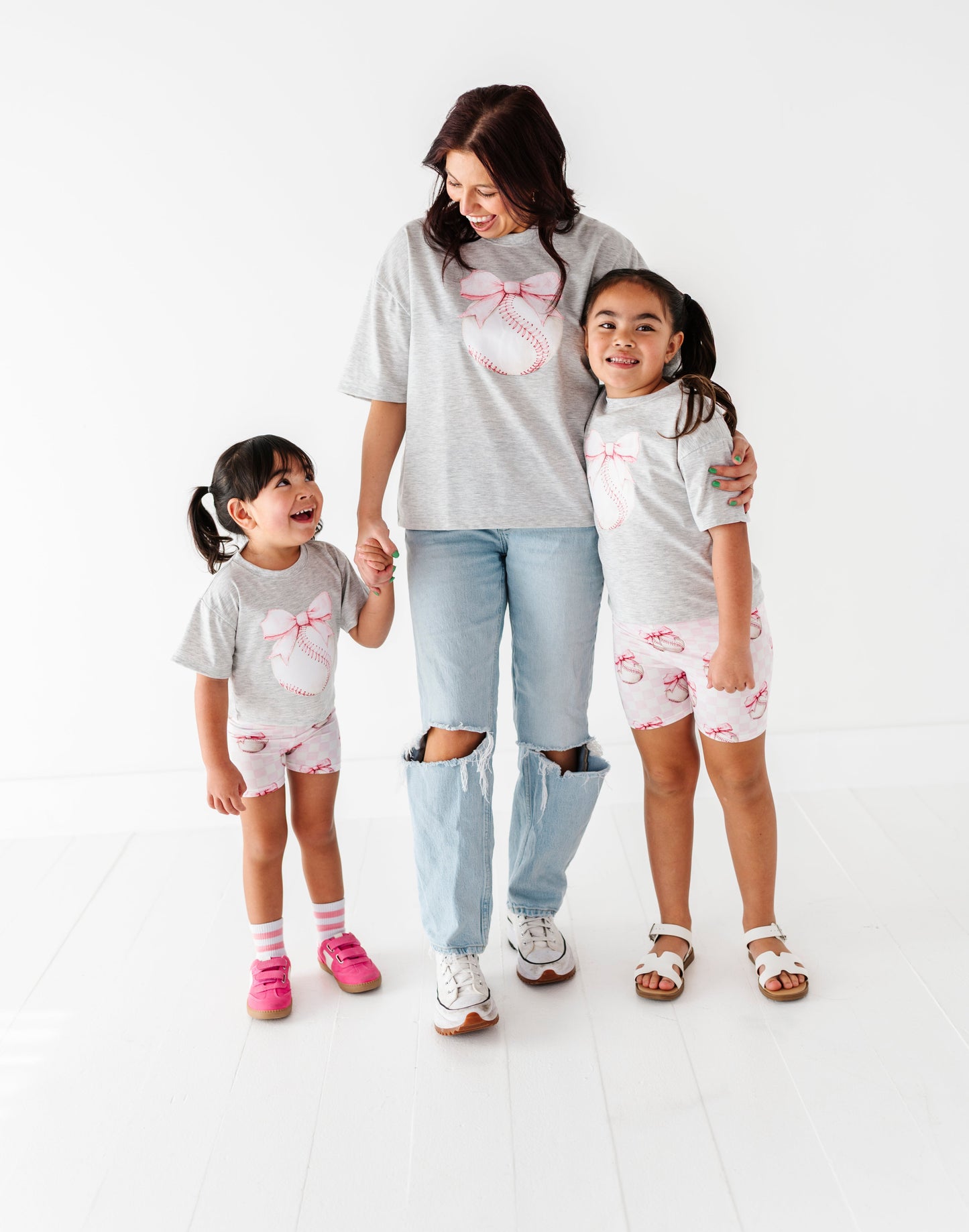 Woman and two children wearing matching outfits with a pink bow and baseball design on a white background