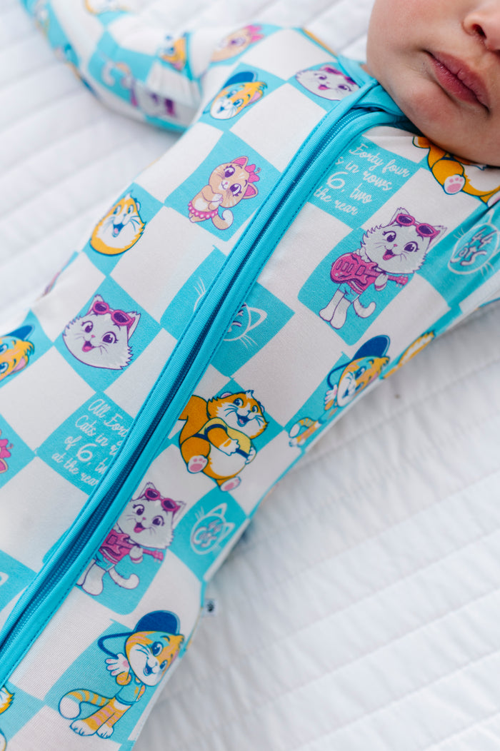 Child wearing a patterned romper with 44 Cats characters on a white quilted surface