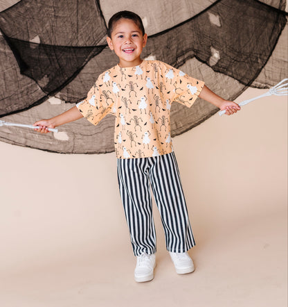 Child wearing a patterned shirt and striped pants standing in front of a netted backdrop.