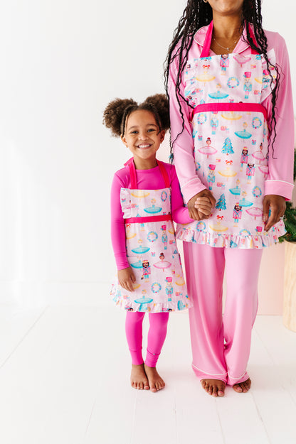 A little girl and her mom wearing matching Christmas aprons featuring ballerinas, nutcrackers, trees, presents, and wreaths 