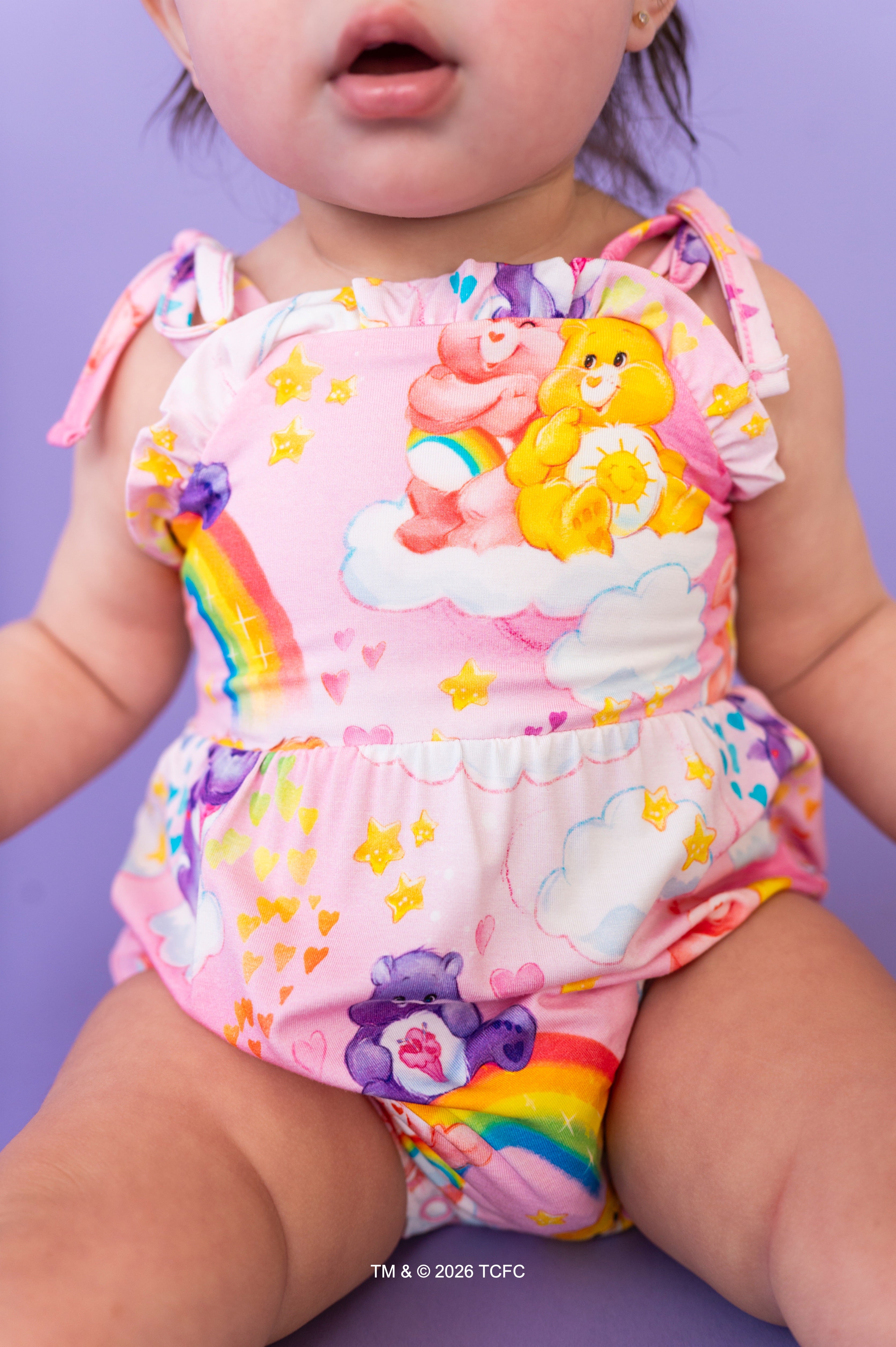 Child wearing a colorful rainbow-themed romper with Care Bears on a purple background