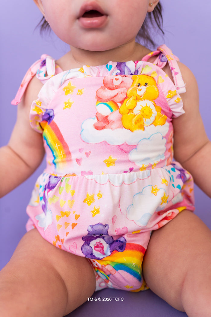 Child wearing a colorful rainbow-themed romper with Care Bears™ on a purple background