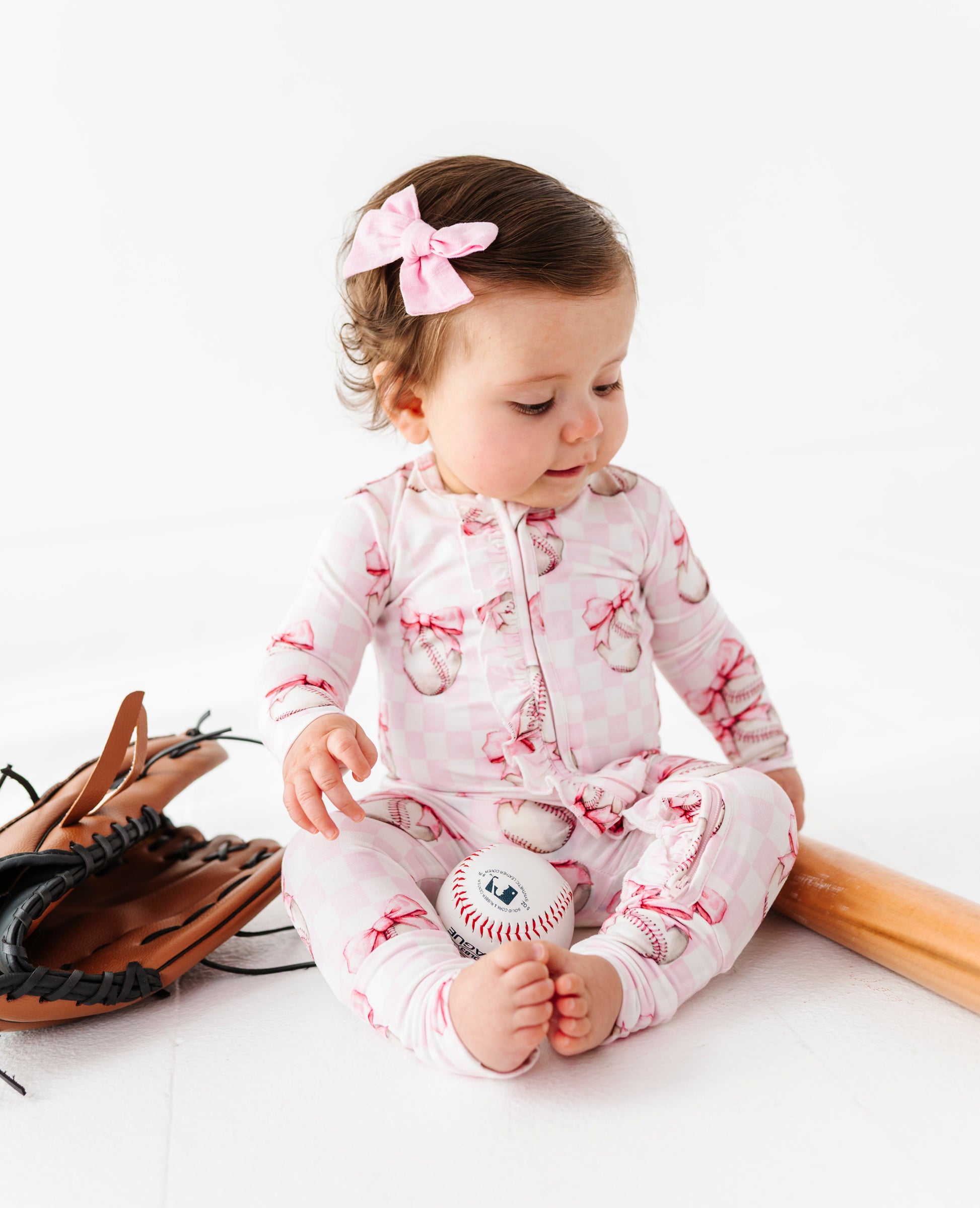 Baby in a pink bamboo outfit with a bow, sitting on a white surface.
