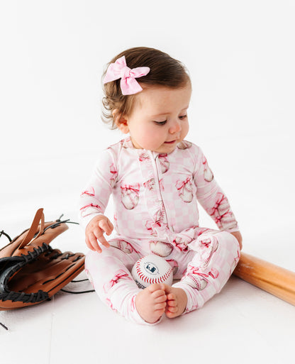 Baby in a pink bamboo outfit with a bow, sitting on a white surface.