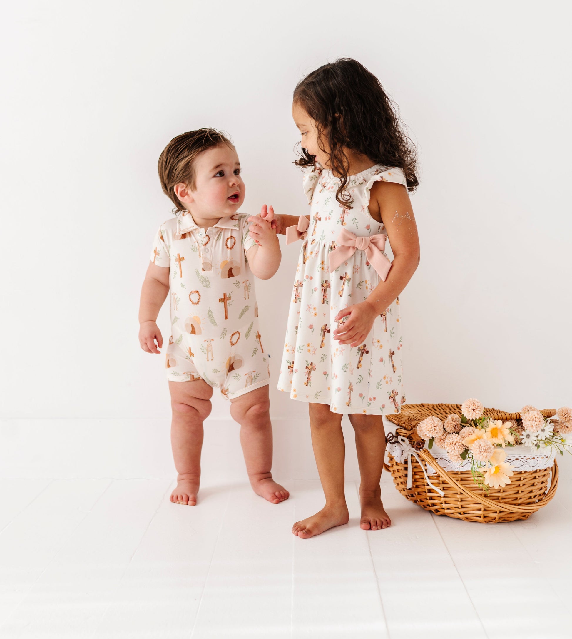 Two children in matching Easter outfits standing next to a basket of flowers on a white background