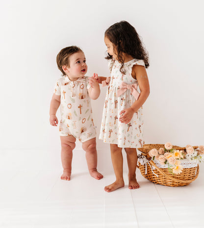 Two children in matching Easter outfits standing next to a basket of flowers on a white background