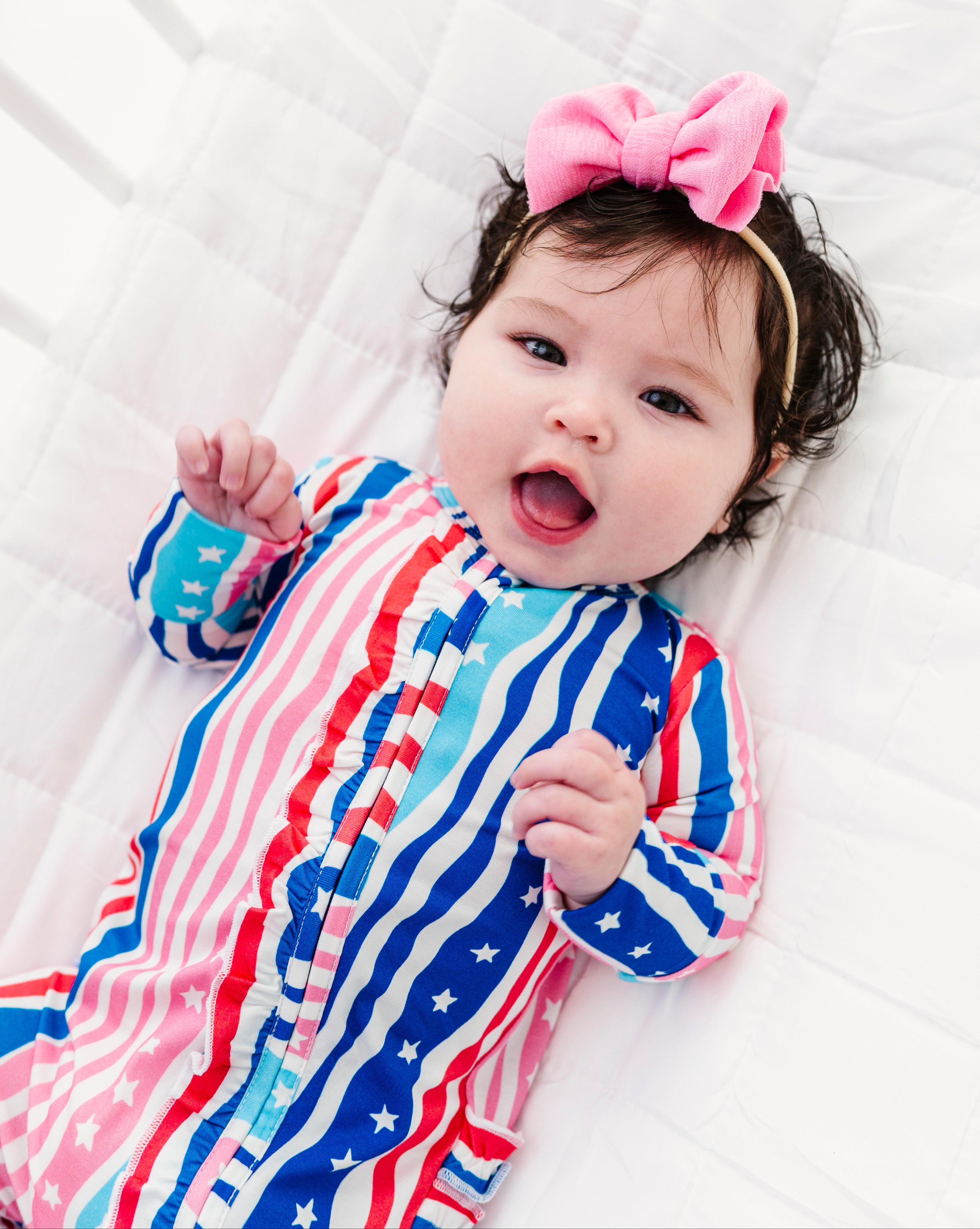 Baby wearing a colorful bamboo zip romper with a pink bow headband on a white background