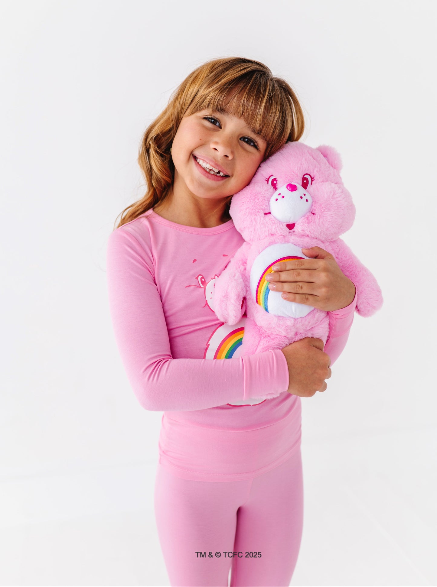 Child holding Cheer Bear plush while wearing matching Care Bears pajamas