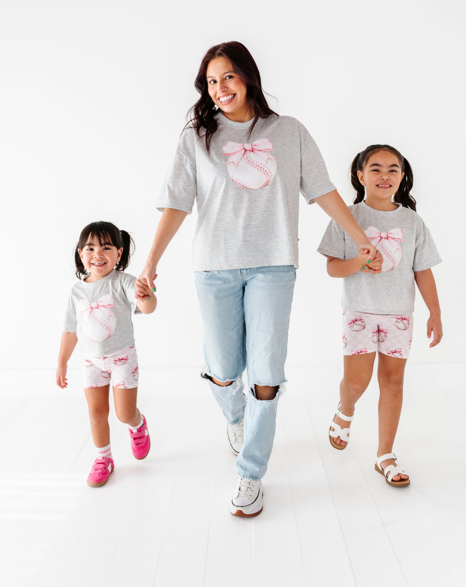 Woman and two children wearing matching gray t-shirts with baseball graphics on a white background