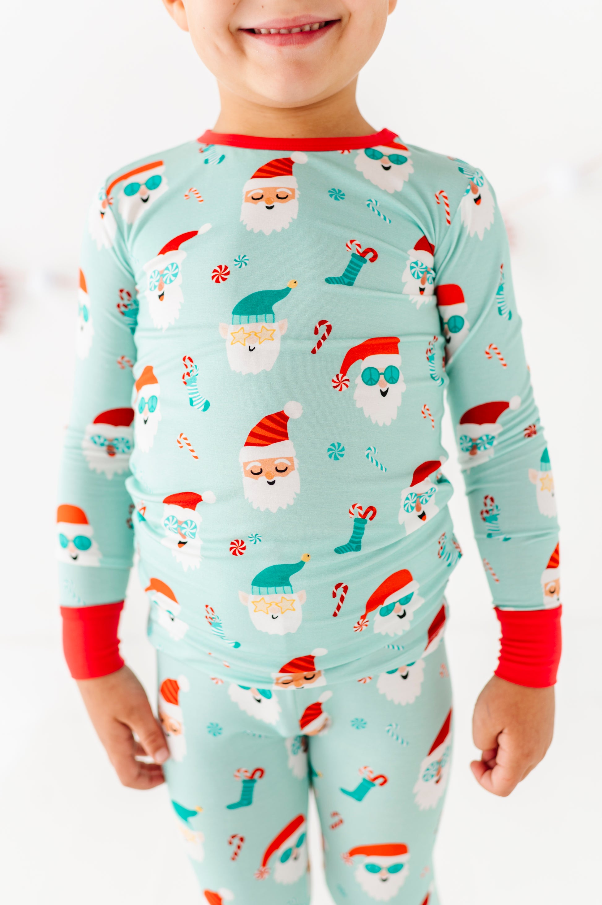 Child wearing a festive bamboo pajama set with Santa Claus and Christmas-themed designs on a light blue background.